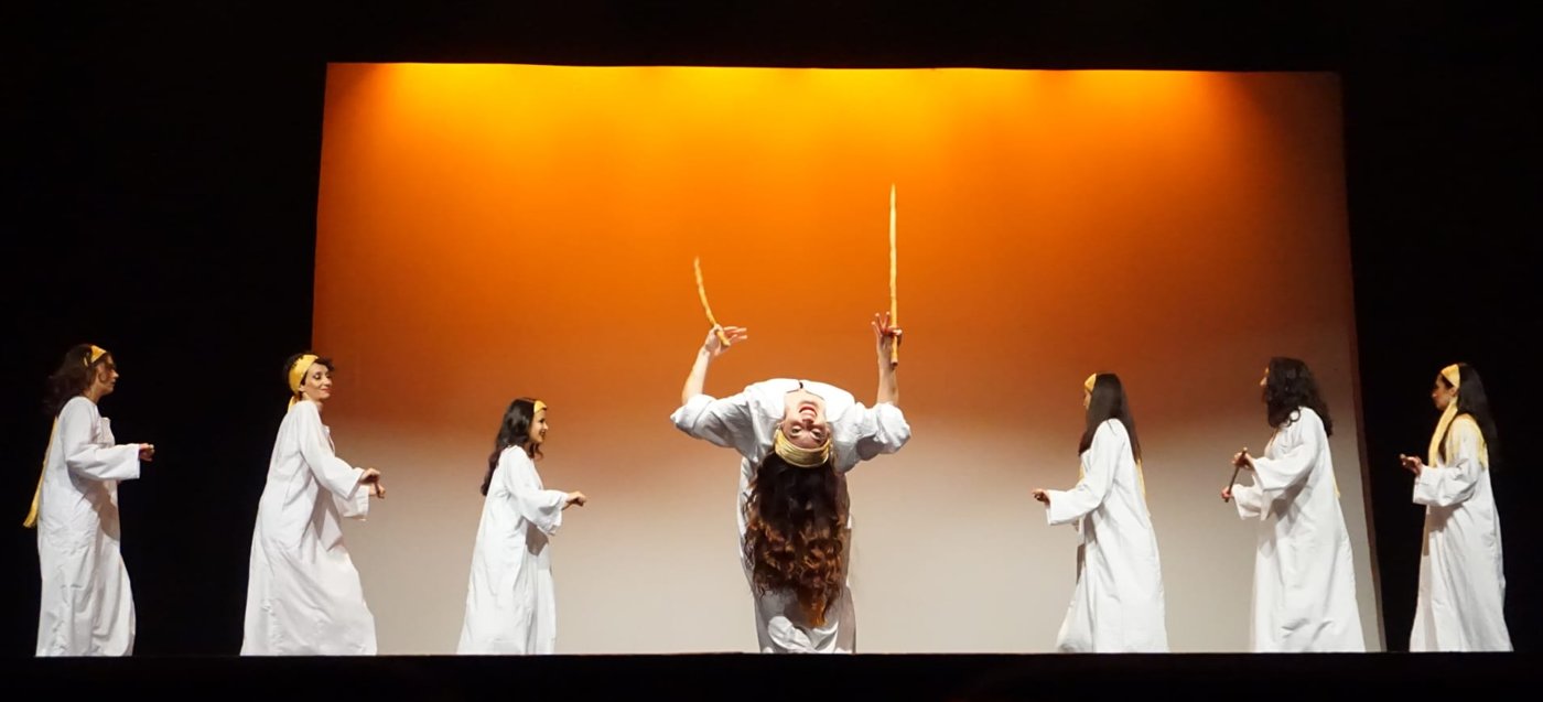 Tableau saïdi : Ciya cambrée, bâtons levés, entourée des danseuses en galabeya blanche